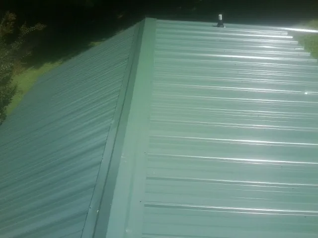 New green metal panels meeting at the ridge of a roof — Flat Roof Repair work by our crew in Roxbury